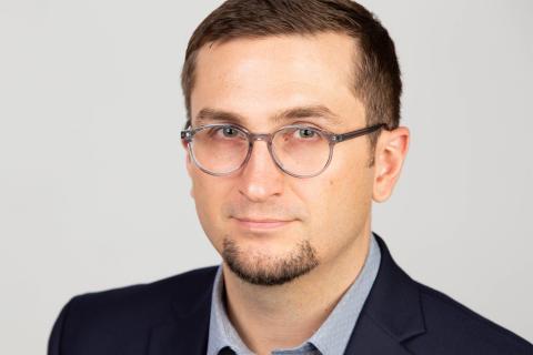 Erick Amick, a male-presenting person who smiles towards the camera against a light-gray background.